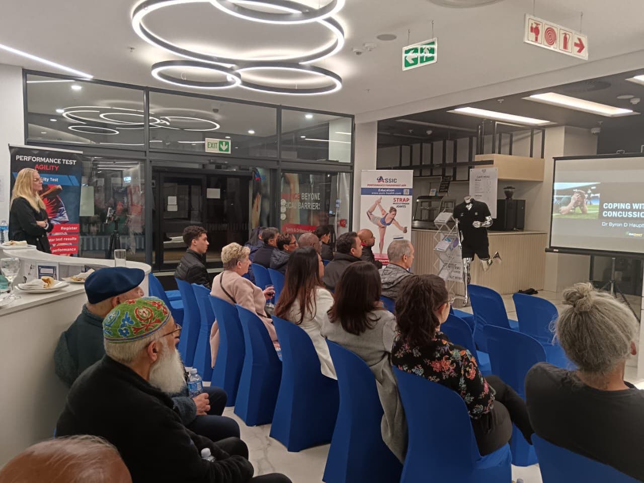 Audience on blue seating listening to a talk on coping with concussion at a MedTalk Network event